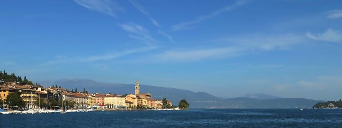 Trip Unterkunft beliebte Urlaubsziele am Gardasee -  Mit einer Fläche von 370 km² ist der Gardasee der größte See Italiens. Es liegt am Fuße der Alpen und erstreckt sich über drei Staaten: Lombardei, Venetien und Trentino. Die maximale Tiefe des Sees beträgt 346 m, er hat eine längliche Form und sein nördliches Ende ist sehr schmal. Dort ist der See von den Bergen der Gruppo di Baldo umgeben. Du trittst aus deinem gemütlichen Hotelzimmer und es begrüßt dich die warme italienische Sonne. Du blickst auf den atemberaubenden Gardasee, der in zahlreichen Blautönen schimmert - von tiefem Dunkelblau bis zu funkelndem Türkis. Majestätische Berge umgeben dich, während die Brise sanft deine Haut streichelt und der Duft von blühenden Zitronenbäumen deine Nase kitzelt. Du schlenderst die malerischen, engen Gassen entlang, vorbei an farbenfrohen, blumengeschmückten Häusern. Vereinzelt unterbricht das fröhliche Lachen der Einheimischen die friedvolle Stille. Du fühlst dich wie in einem Traum, der nicht enden will. Jeder Schritt führt dich zu neuen Entdeckungen und Abenteuern. Du probierst die köstliche italienische Küche mit ihren frischen Zutaten und verführerischen Aromen. Die Sonne geht langsam unter und taucht den Himmel in ein leuchtendes Orange-rot - ein spektakulärer Anblick.